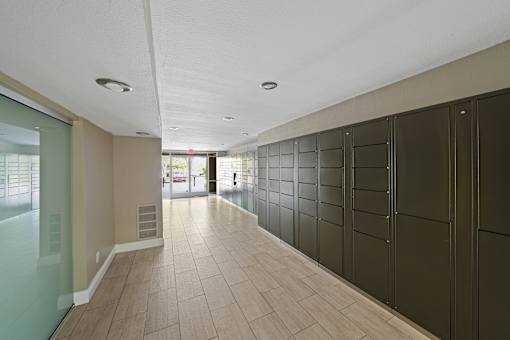 A long hallway with a glass door on the left and a wall of black lockers on the right.
