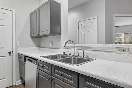 A kitchen with a white counter top and grey cabinets.
