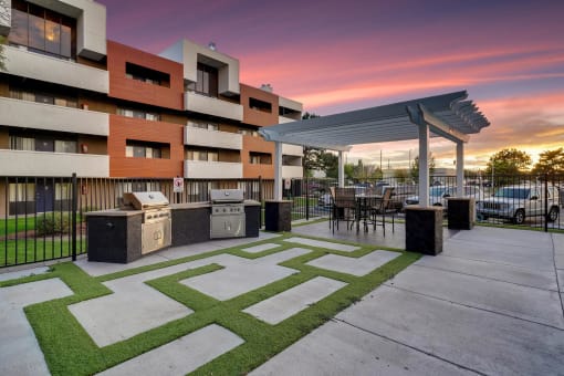 a patio with a grill and a building with a sunset in the background
