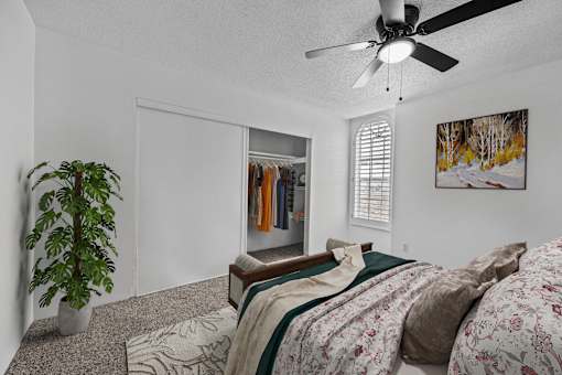A bedroom with a bed, a ceiling fan, and a plant.