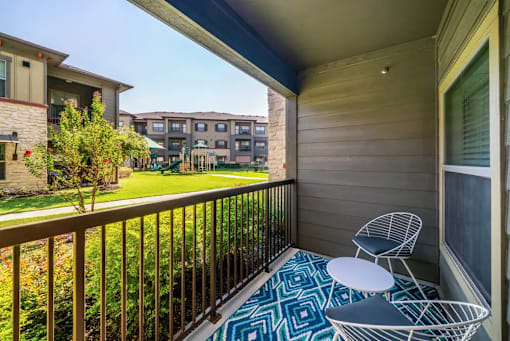 A balcony with a table and chairs overlooking a grassy area.