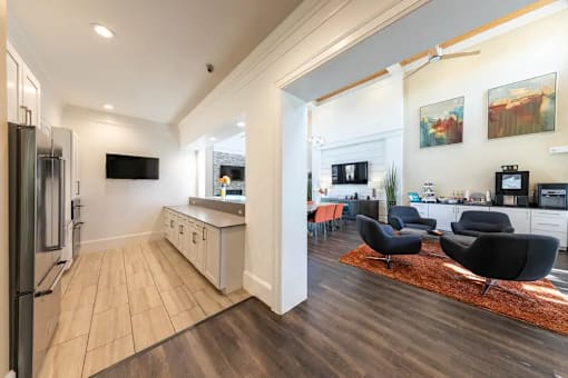 A modern kitchen with a refrigerator on the left and a living room area with a couch and chairs on the right.