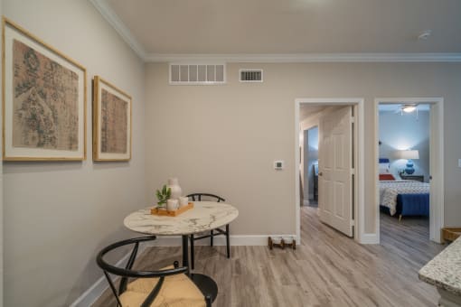 a small table with two chairs in the corner of a room with a bedroom in the background