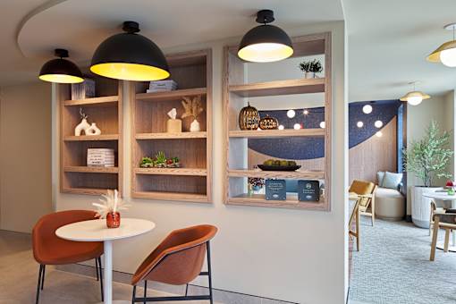 A modern dining area with a white table, chairs, and shelves with decorative items.