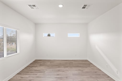 an empty room with white walls and wood floors and two windows