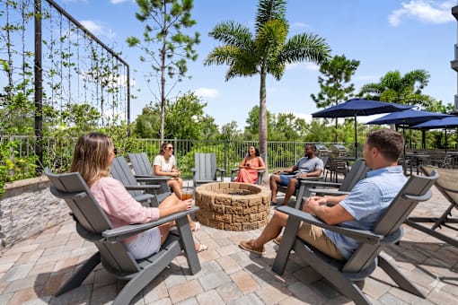 A group of people are sitting around a fire pit on a patio.