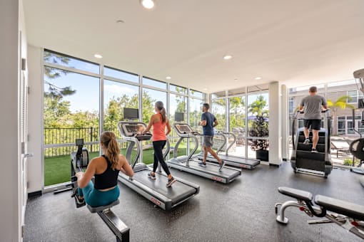 A woman is working out on a treadmill in a gym with other people.