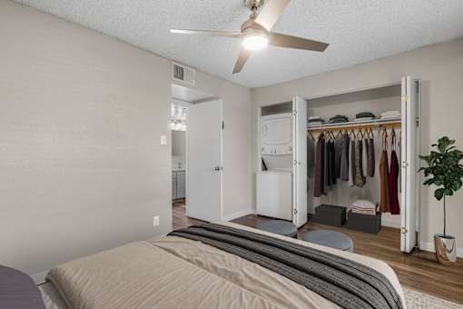 A bedroom with a bed, a ceiling fan, and a closet with clothes.
