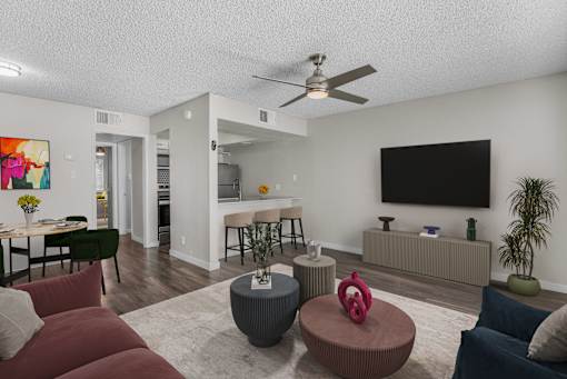 A living room with a red couch, a grey ottoman, and a television on the wall.