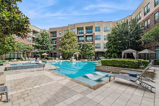 A large swimming pool surrounded by a brick patio and lounge chairs.
