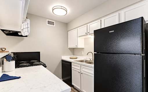 A black refrigerator stands in a kitchen with white cabinets and a marble countertop.