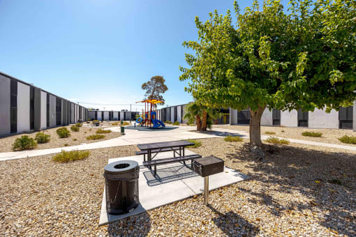 a playground with a picnic table and a tree in front of a building