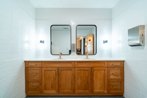 two mirrors on top of a bathroom counter with two sinks