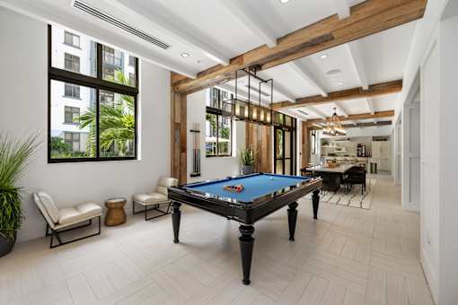 A pool table is in the middle of a room with a view of a building outside the window.