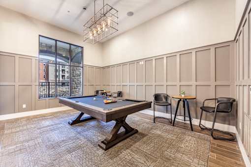 A room with a pool table and chairs.