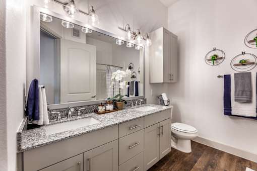 A bathroom with a large mirror, a sink, a toilet, and a cabinet.