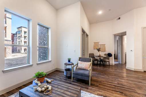 A living room with a grey couch, a coffee table with a plant and some shells on it, and a view of a street through the windows.