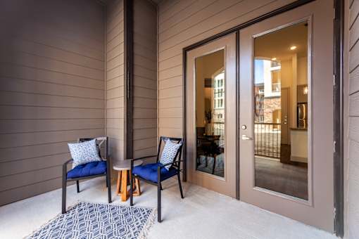 Two chairs and a table are on a porch.