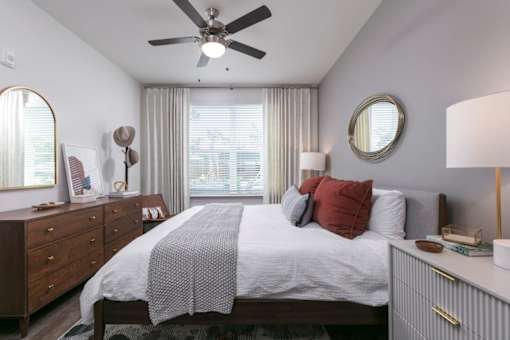 A bedroom with a bed, dresser, mirror, and window.