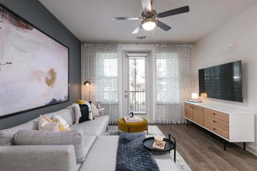 A living room with a grey couch, a yellow ottoman, and a large painting on the wall.