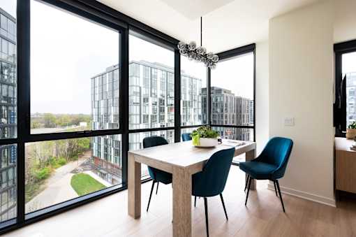 A modern dining room with a table and chairs and a view of a cityscape through the windows.