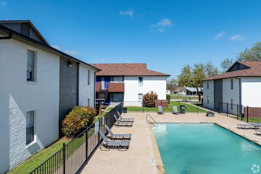 A swimming pool surrounded by a fence and chairs in a sunny day.