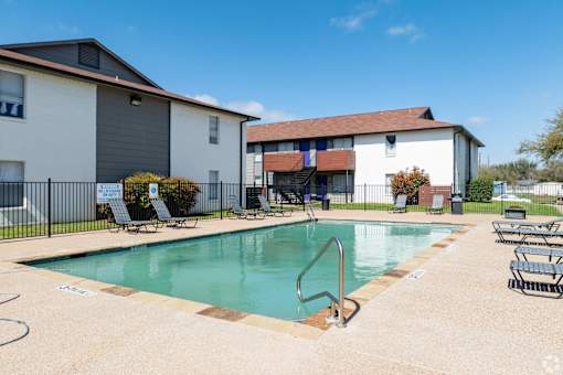 A swimming pool surrounded by lounge chairs and a building in the background.