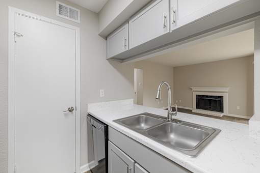 A white door is on the left of a kitchen with a stainless steel sink.