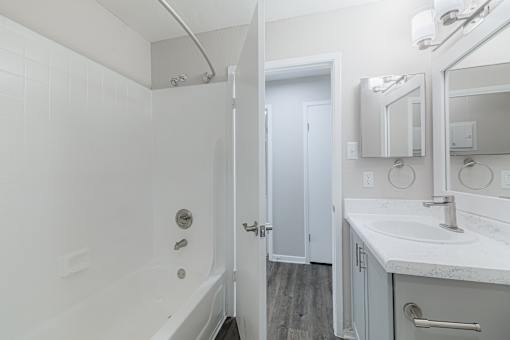 A white bathroom with a sink, mirror, and bathtub.