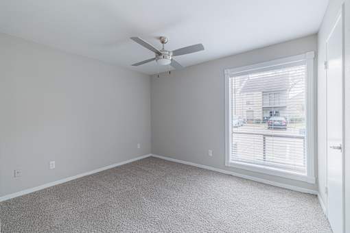 A room with a ceiling fan and a window overlooking a street.