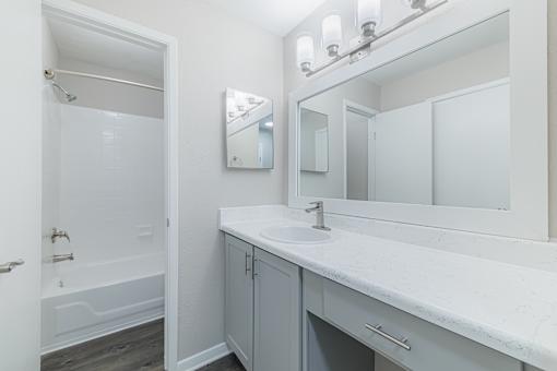 A white bathroom with a sink, mirror, and bathtub.