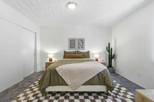A bedroom with a bed, two lamps, and a cactus.