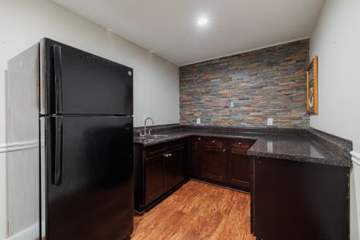 a kitchen with a black refrigerator and a stone wall
