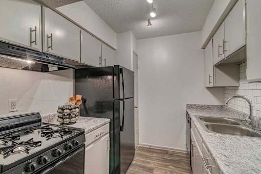 A kitchen with a black refrigerator, white cabinets, and a black gas stove.
