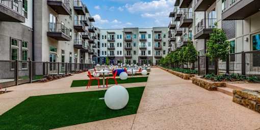 A large white ball is in the middle of a grassy area in front of apartment buildings.