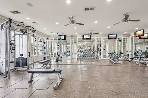 A spacious gym with a variety of equipment and a bench for resting.