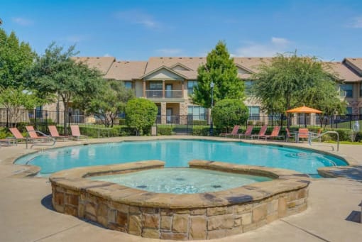 a swimming pool with chairs around it in front of an apartment building