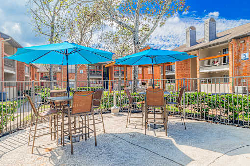 A patio with chairs and umbrellas in front of a brick building.