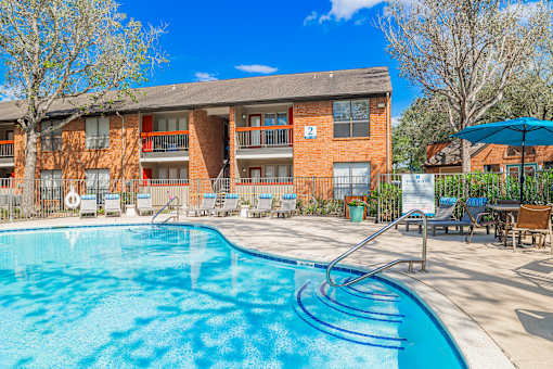 A swimming pool in front of a brick building with a blue umbrella.