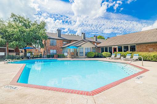 A large swimming pool in front of a house with a red brick exterior.