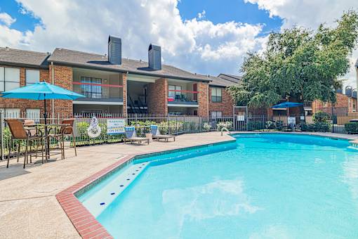 A large swimming pool in front of a building with a blue sky and clouds in the background.