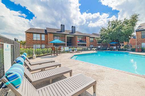 A pool area with sun loungers and a building in the background.