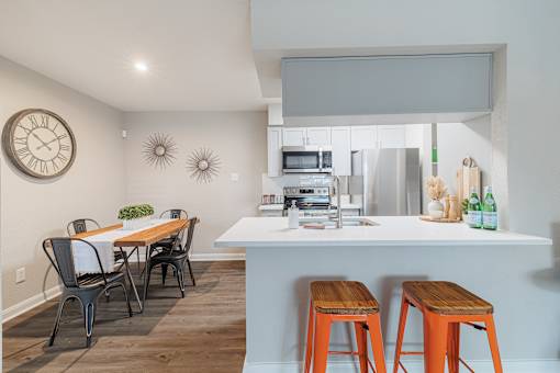 A kitchen with a table and chairs in the foreground and a clock on the wall.