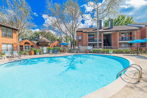 A large swimming pool in front of a building with a blue sky and clouds in the background.