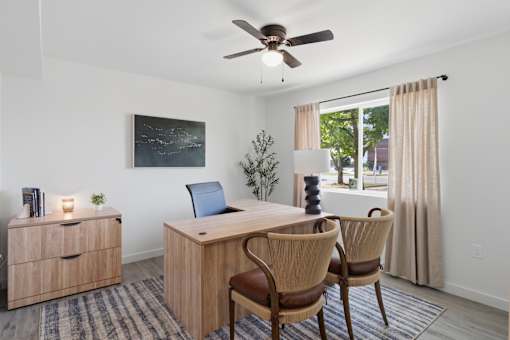 A room with a desk, chairs, and a ceiling fan.