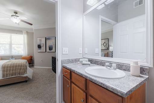 A bathroom with a sink, mirror, and a bedroom with a bed.