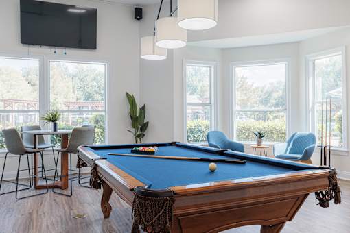 A pool table is in the middle of a room with a TV and a chair.