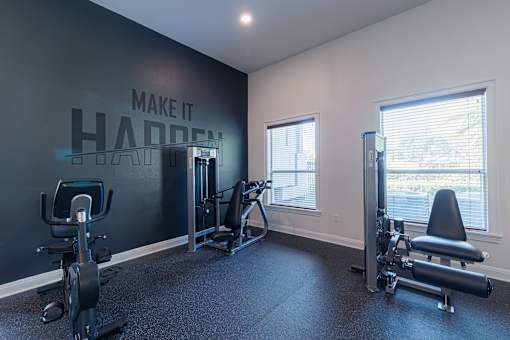 A gym with a wall that says "make it happen" and a row of exercise equipment.