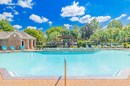 A large swimming pool surrounded by a brick patio and a gazebo in the background.