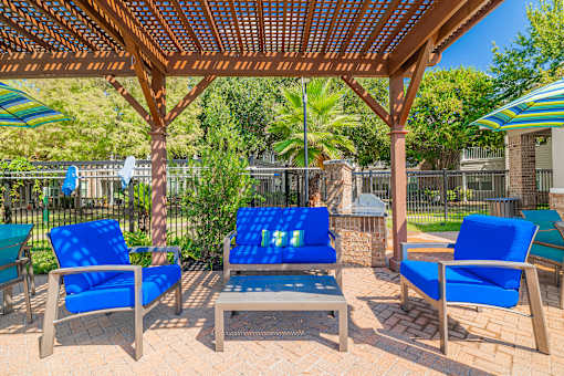 A wooden pergola with blue cushioned chairs and a bench.